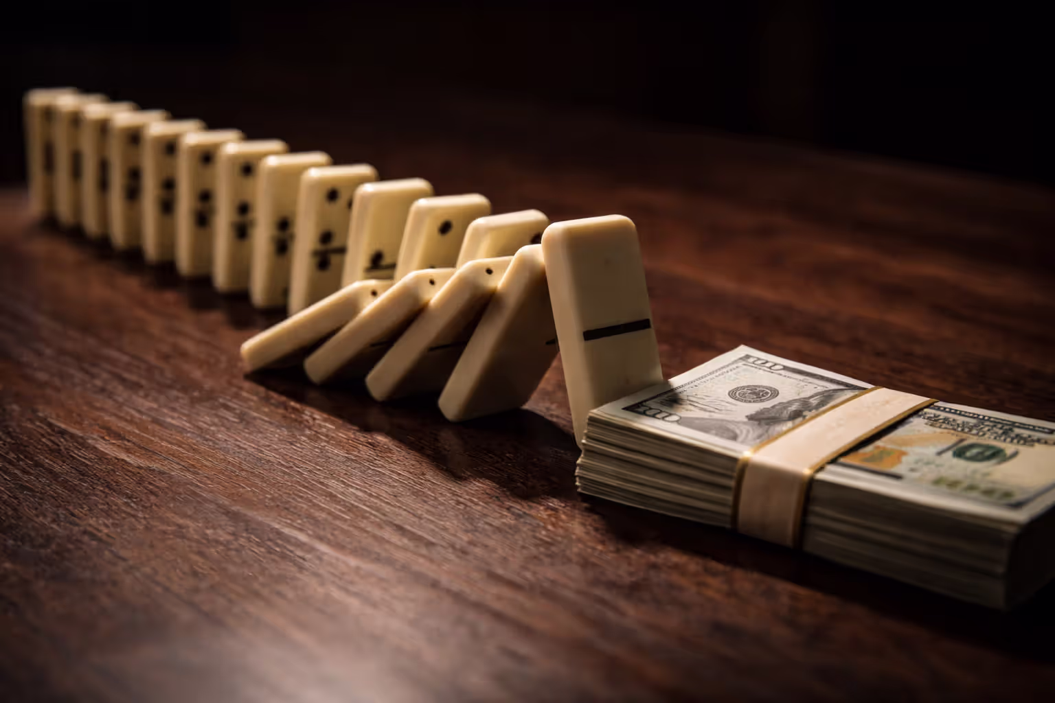Falling dominoes about to knock over a stack of dollar bills representing cascading legal compliance failures